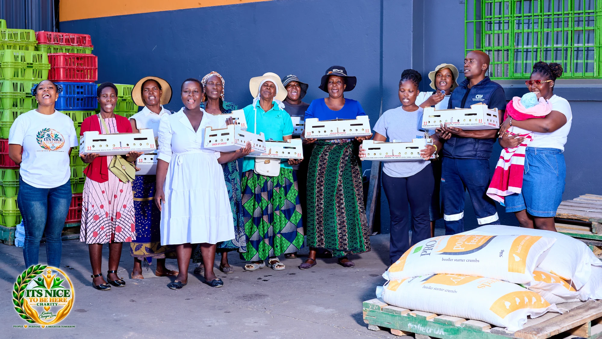 Community members holding chick boxes beside bags of poultry feed in Harare